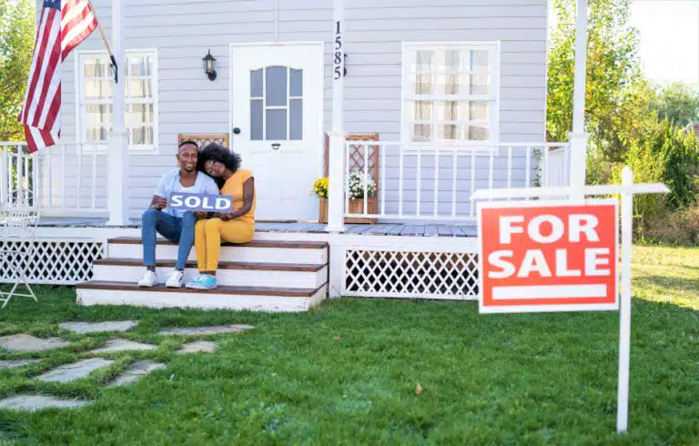 couple holding sold sign outside of house