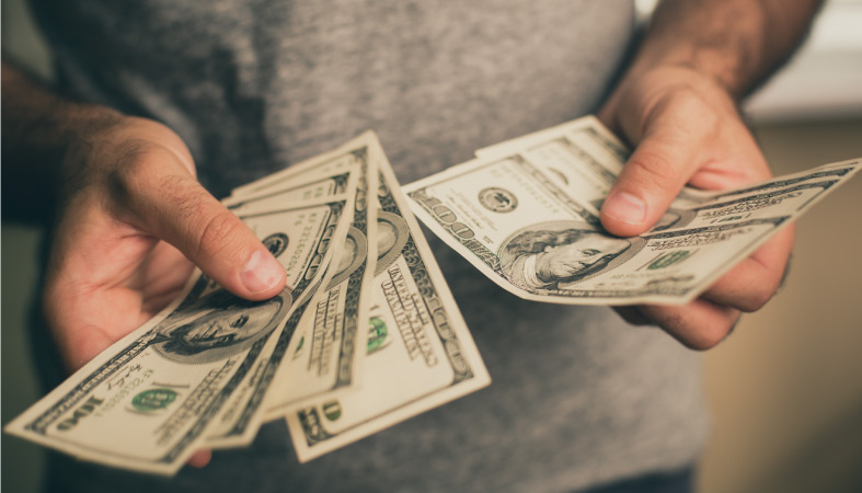 A close-up view of a man holding several $100 bills in his hands. 