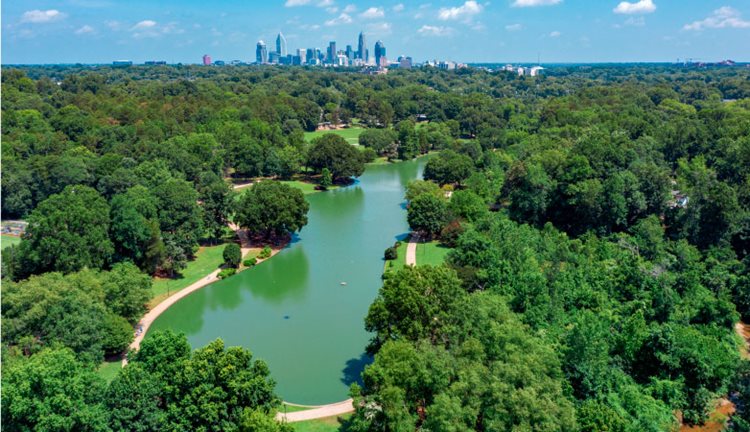 Aerial view of the lake and walking path of Freedom City Park in Charlotte, with the city’s distinct skyline visible in the distance. The picturesque skyline is one of the perks of living in Charlotte, NC.