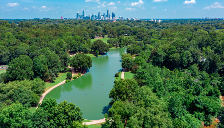 A bird’s-eye view of the lake and walking path of Freedom City Park in Charlotte, with the city’s distinct downtown skyline visible in the distance.