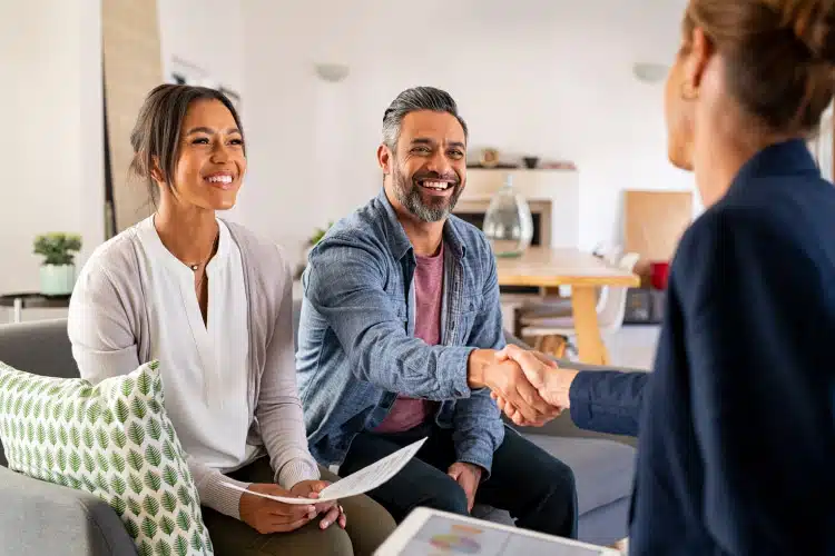 A couple shakes hands with a real estate agent after negotiating their house offer