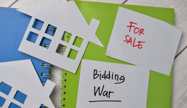 Sticky notes sit on top of a green notebook. One note reads “For Sale,” and the other reads “Bidding War”