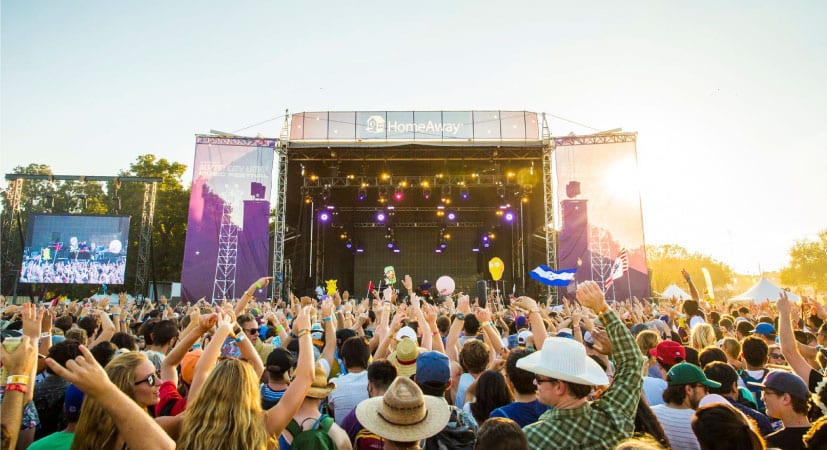An excited crowd is gathered in front of a huge outdoor stage, watching a live performance at the Austin City Limits Music Festival.