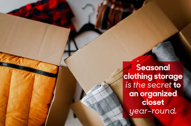 Top-view of two cardboard boxes, packed with winter clothes. A red square with overlaid white text reads “Seasonal clothing storage is the secret to an organized closet year-round.”