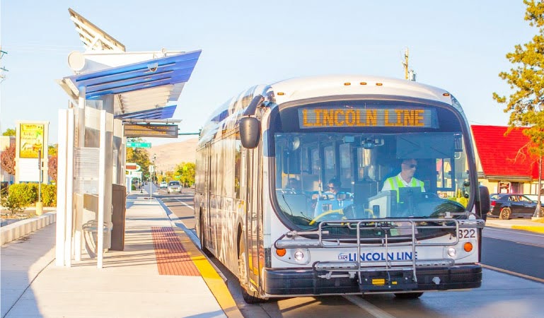 An RTC bus is waiting at a bus stop in Reno, Nevada, on a sunny day. The digital sign at the front of the bus reads, “Lincoln Line,” indicating which route it's traveling on.