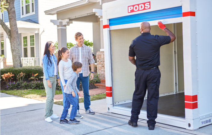 A PODS driver shows a family of four the inside of their PODS portable storage container, which he has just delivered to their driveway. They’re planning to use it to store furniture and equipment during their home remodel.