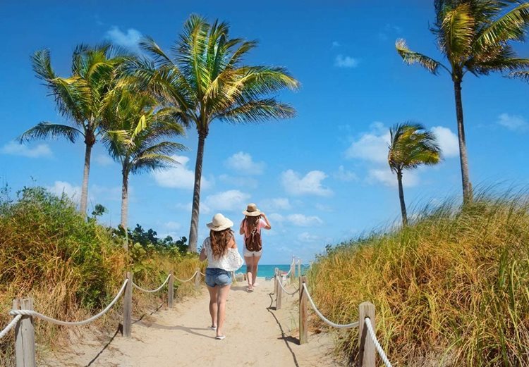 Two women walk on a beach path toward the Atlantic.