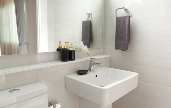 The corner of a half bathroom with a matching white toilet and pedestal sink. The wall behind the toilet and sink features a wide mirror and a floating marble shelf. 