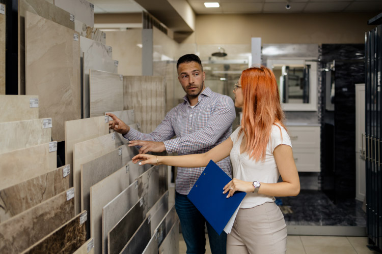 A man is speaking with a salesperson in a bathroom remodeling showroom. They’re looking at samples of bathroom tiles.