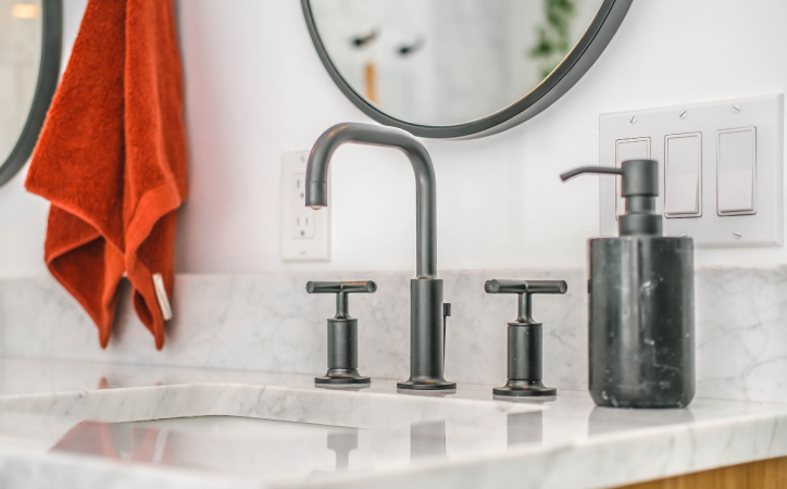 A bright orange hand towel hangs above a light gray marble bathroom counter. The hand towel gives a pop of color to the otherwise muted half bath.