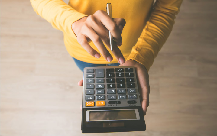 A person holding a calculator and a pen is using the 5% Rule to help determine if renting or buying is the best choice for them.