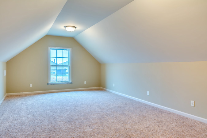 A renovated attic with a full-sized window, wall sockets, and newly installed carpet.