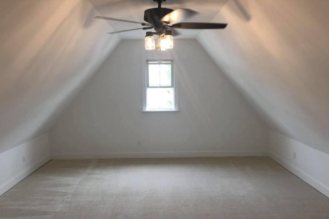 A recently renovated attic with white walls, new carpet, and a ceiling fan to keep the space cool.