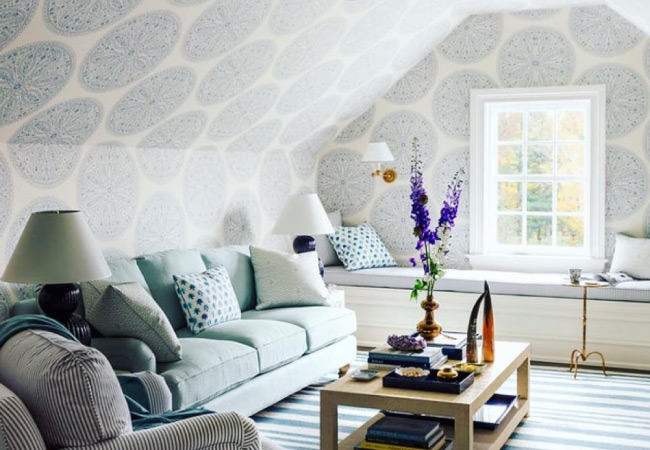 A finished attic with a boldly patterned wallpaper and complementary furniture in blue, green, and white hues.