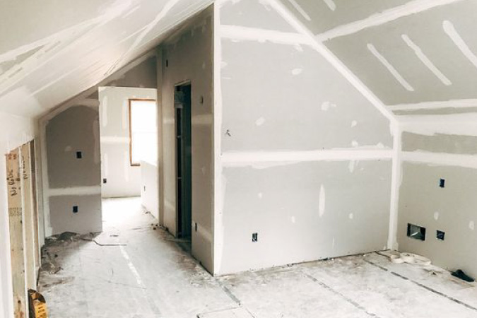 An attic that has been partially remodeled. The drywall has been installed and the floor is covered in construction dust.