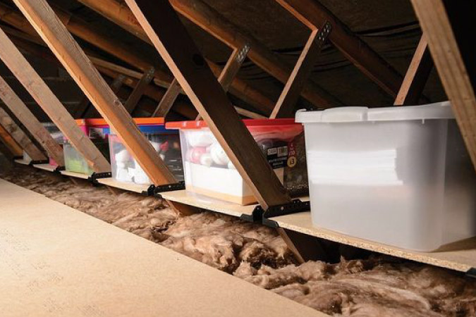 Several plastic storage tubs are positioned on shelves built into attic trusses.