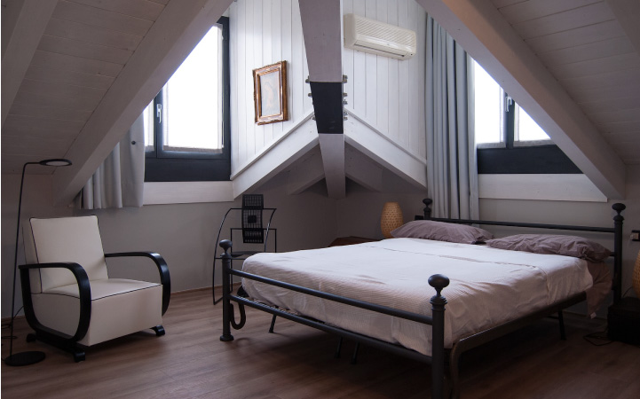 An attic that's been renovated into a chic bedroom with black and white decor. Windows on either side of a corner rafter are letting natural light into the room.