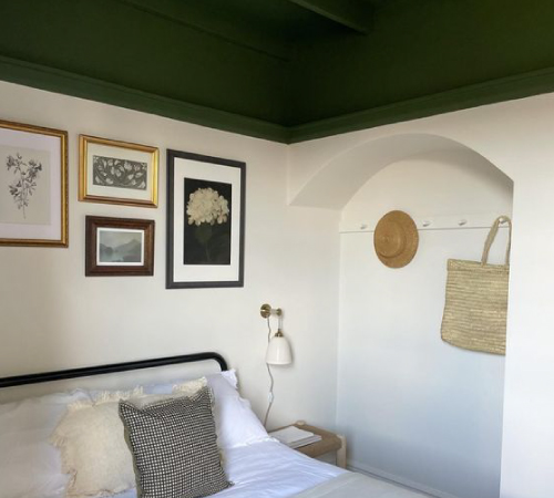 A small attic bedroom with white walls and linens features a dark green ceiling for a pop of personality.