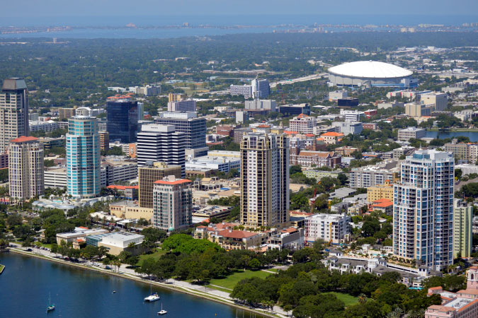 Aerial view of St. Petersburg, Florida, featuring the waterfront, several tall buildings, and a sports arena.