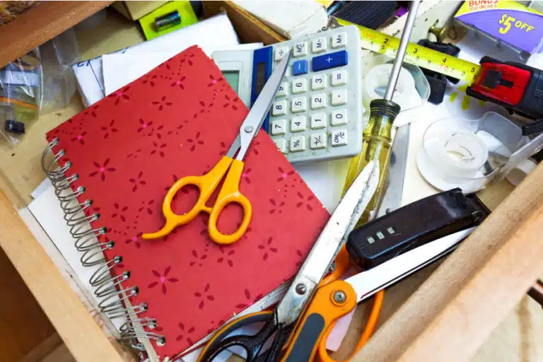 A cluttered mess of a junk drawer, with three pairs of scissors, a notebook, screwdriver, calculator, and other assorted odds and ends.
