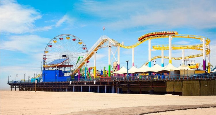 View of the colorful roller coaster and ferris wheel on Santa Monica Pier on a sunny day in Santa Monica, California.
