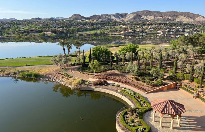 An aerial view of the Lake Las Vegas community on a sunny day, featuring beautifully landscaped public spaces, a tranquil lake, and mountain views.