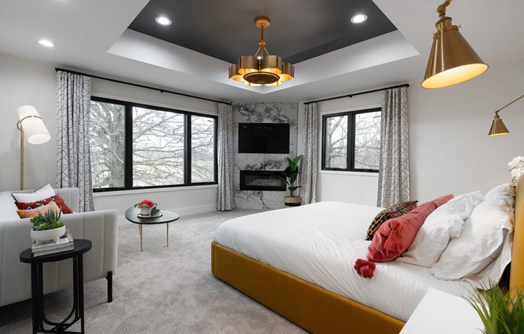 A modern bedroom with gray walls, a stone slab wall with mounted TV and built-in fireplace, and an orange bed as an accent.