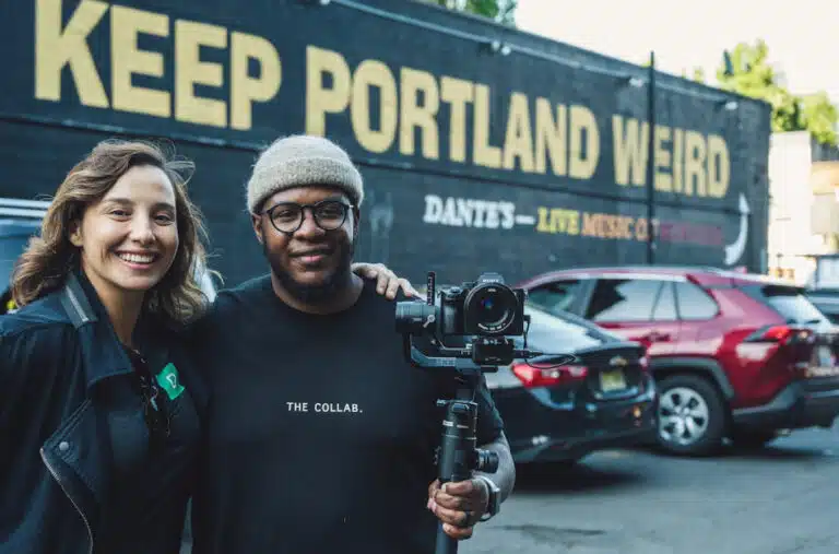 A pair of photographers stand in front a "Keep Portland Weird" mural