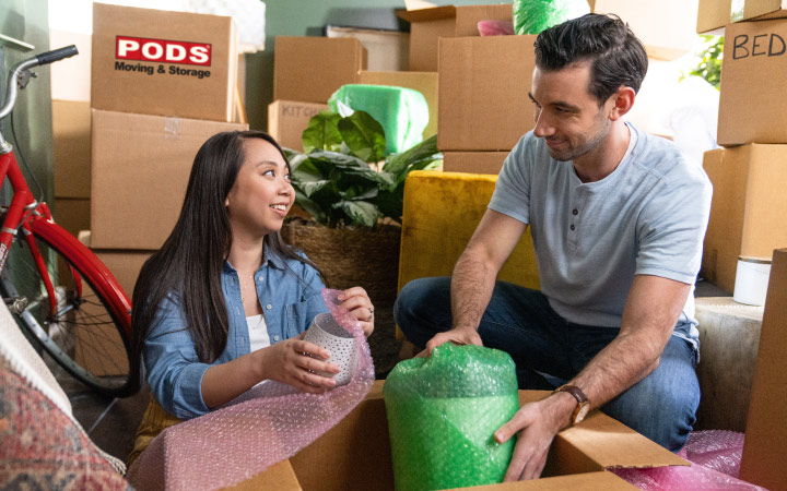 A couple is wrapping fragile items in bubble cushioning roll and packing them in moving boxes for their out-of-state move