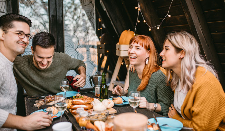 Friends are smiling and laughing around the dinner table, saying their final farewells before one of them makes a long-distance move to another city.