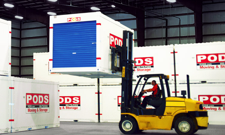 A forklift driver skillfully positions a ӰPro storage container for placement atop another container in a secure ӰPro storage facility.