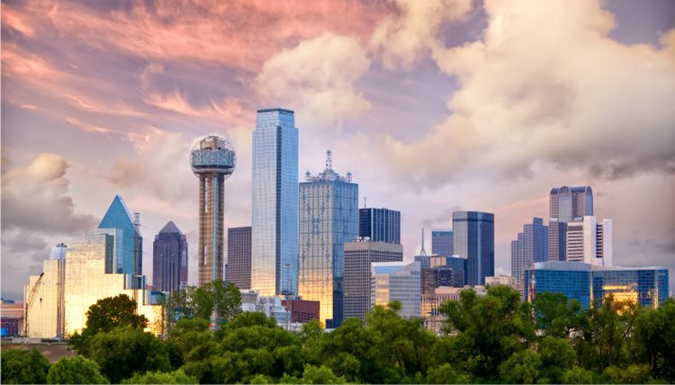 The Dallas, Texas, skyline at sunset. Big, puffy clouds hang over Dallas as the soft light from the sunset reflects off the glass skyscrapers in the city.