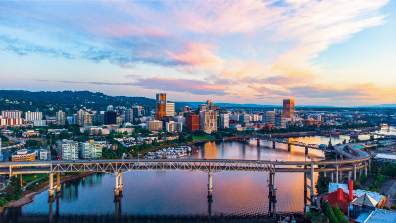 Sunrise over Portland, Oregon. The city looks quiet and the river waters are nearly still, as they reflect the light pink clouds in the early morning.