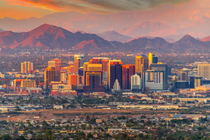 View of Downtown Phoenix, Arizona, during sunset, with an impressive mountain range visible in the background.