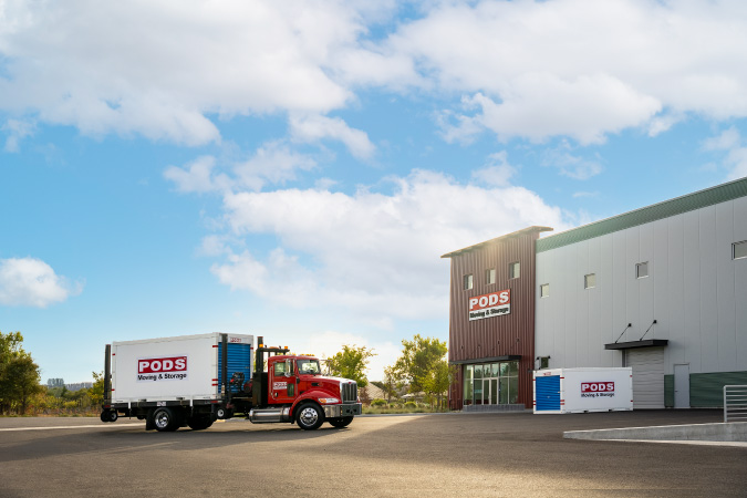 A PODS truck with a PODS portable moving container on its bed arrives at a PODS secure storage center.