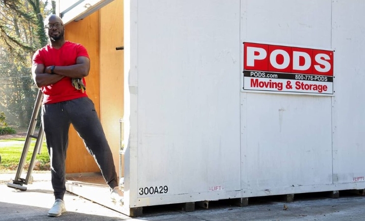 A man is standing with his arms crossed beside a PODS portable storage container that he rented to use for temporary on-site storage during a home remodel.