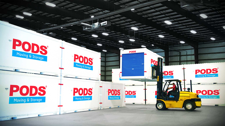 A forklift driver is placing a PODS moving and storage container on top of another one in a secure storage facility. There are several other PODS containers stacked neatly around these.