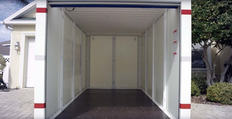 An empty PODS portable storage container sits in a residential driveway, ready to be loaded.