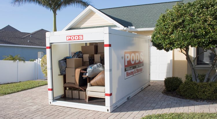 A partially loaded PODS portable storage container in a residential driveway. The container’s door is open and you can see the neatly stacked moving boxes and furniture inside. 