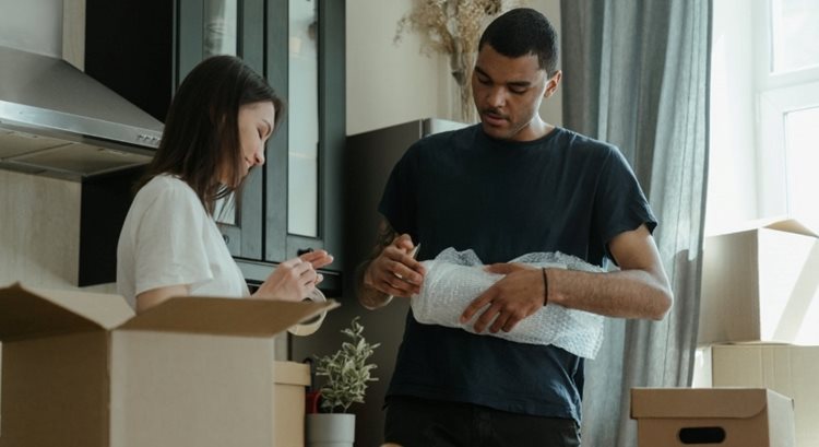 A couple is standing together in their kitchen. They’re carefully packing dishes and other kitchen items in bubble cushioning roll to minimize the risk of damage during their upcoming move.