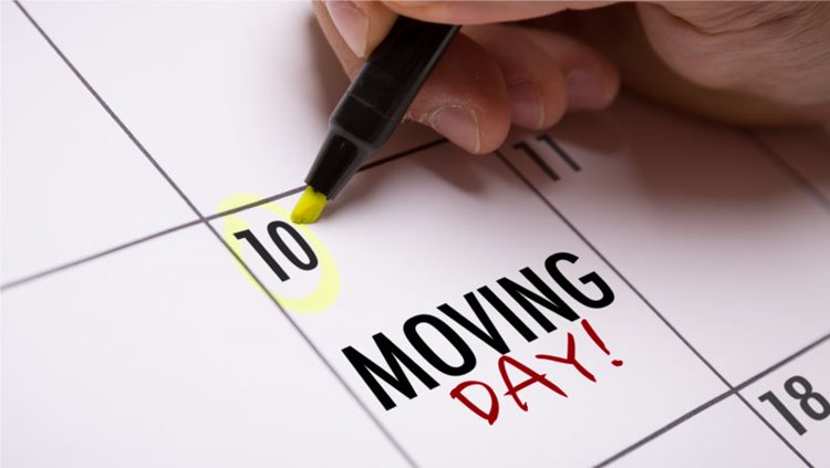 A hand is circling the 10th day of the month on a calendar. There is a note on the same day that says “Moving Day!.”