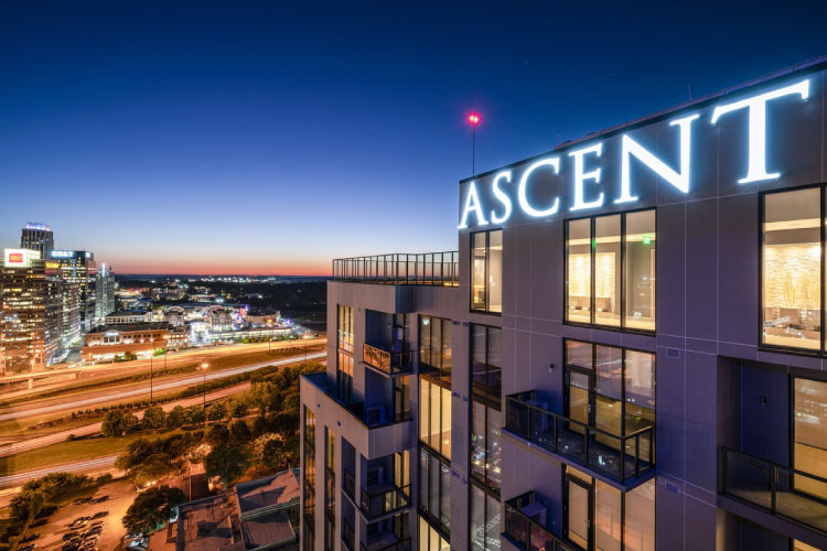 View of the top of the Ascent Midtown luxury Atlanta apartment building at night. The building features illuminated letters at the top, which read “ASCENT.” 