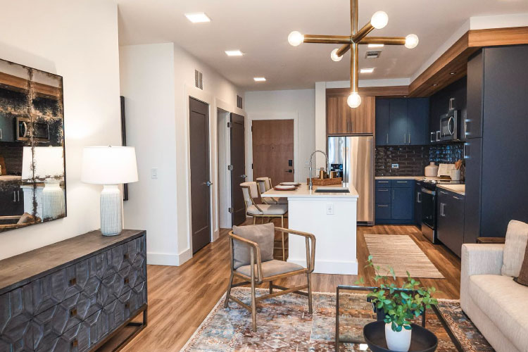 Interior view of an apartment in the Novel Midtown apartment building in Atlanta, Georgia. The apartment features a modern kitchen with a large island, chic lighting fixtures, and wood floors. 