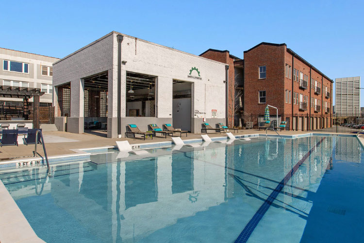 View from the pool at the Smith & Porter Apartments in Atlanta, Georgia. The apartment building features a red brick structure with an adjacent white brick open-air covered patio and community pool.