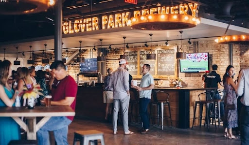 A bunch of locals are socializing at Glover Park Brewery in Marietta, Georgia. There is a sign in lights above the bar that reads "GOLVER PARK". 