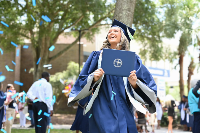 A happy new graduate at the University of North Florida in Jacksonville is walking with her degree as blue confetti is falling nearby