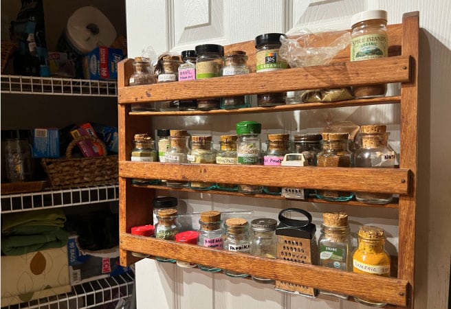 A wooden spice rack filled with spices and hanging on a pantry door.
