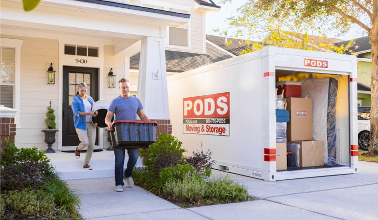 A man and woman are carrying things out of their house to their PODS portable moving container. The container is nearly full and ready for leaving Los Angeles.