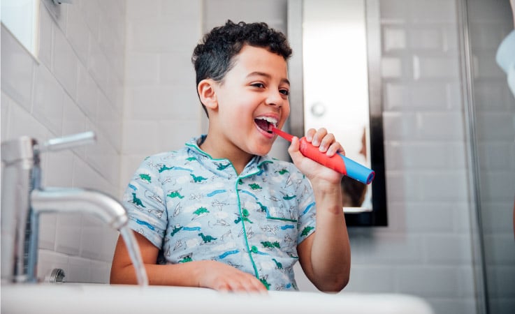 A little boy is brushing his teeth in the bathroom, but he is keeping the water running — wasting water.