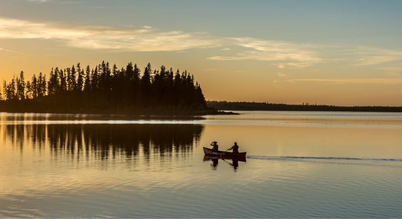 Two people canoeing at dusk near an island in Alberta's Elk Island National Park.

